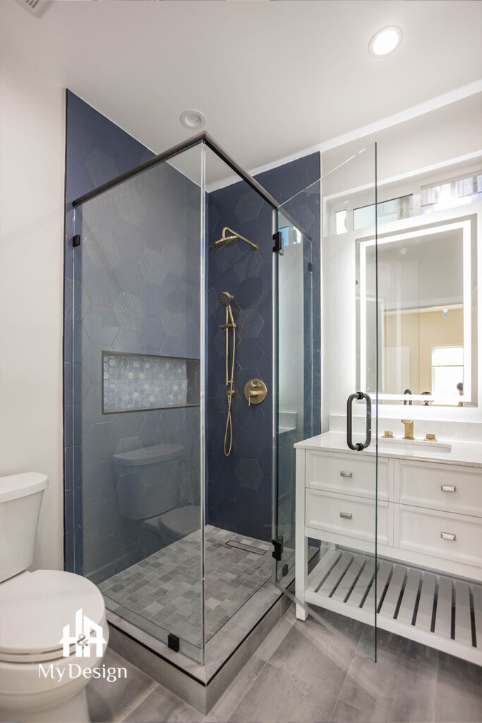 ADU bathroom with a corner glass shower, navy hexagon tile and gold fixtures