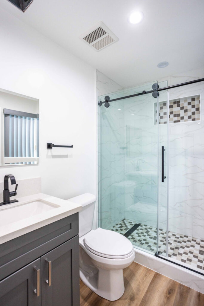 ADU bathroom with a marble-look sliding glass shower, vanity and black fixtures