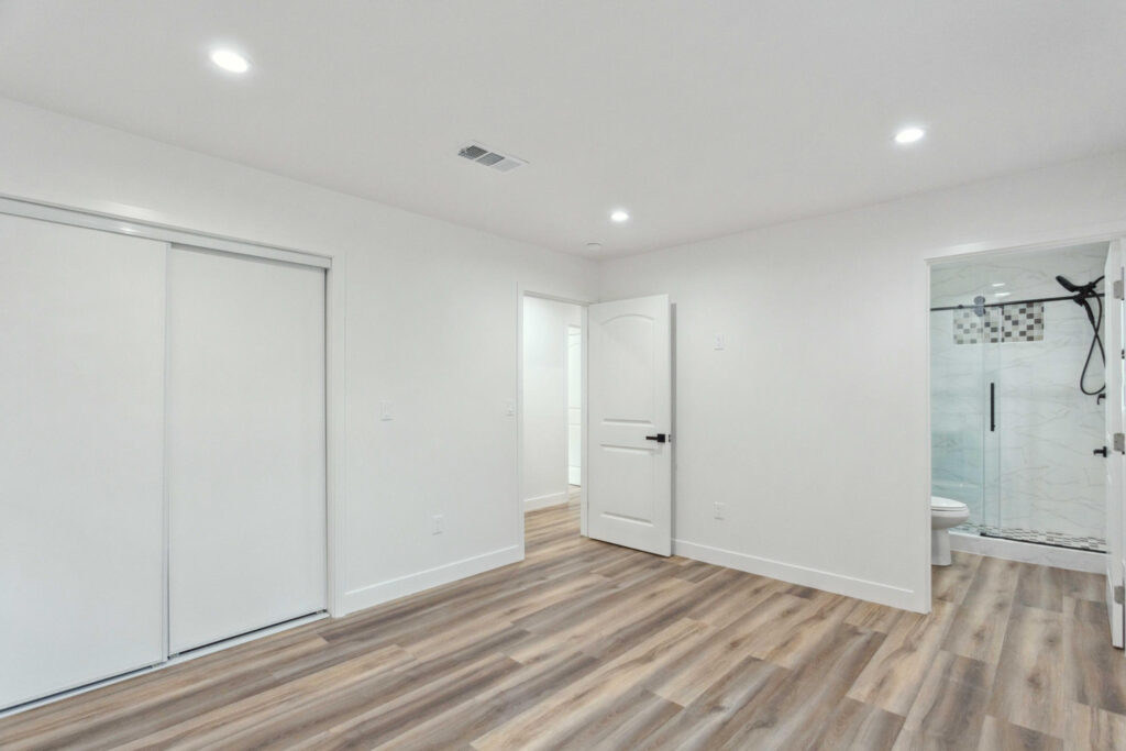 ADU bedroom with sliding closet doors opening through to a bathroom with a glass shower