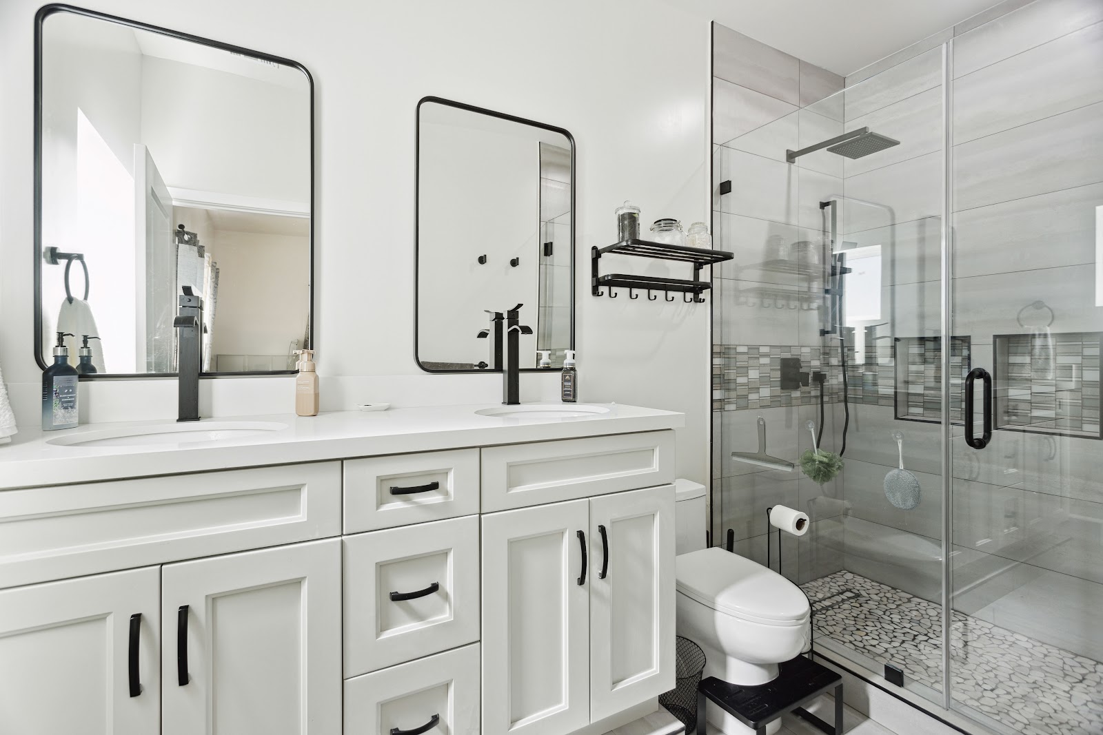 ADU bathroom with a glass shower, black fixtures and framed mirrors