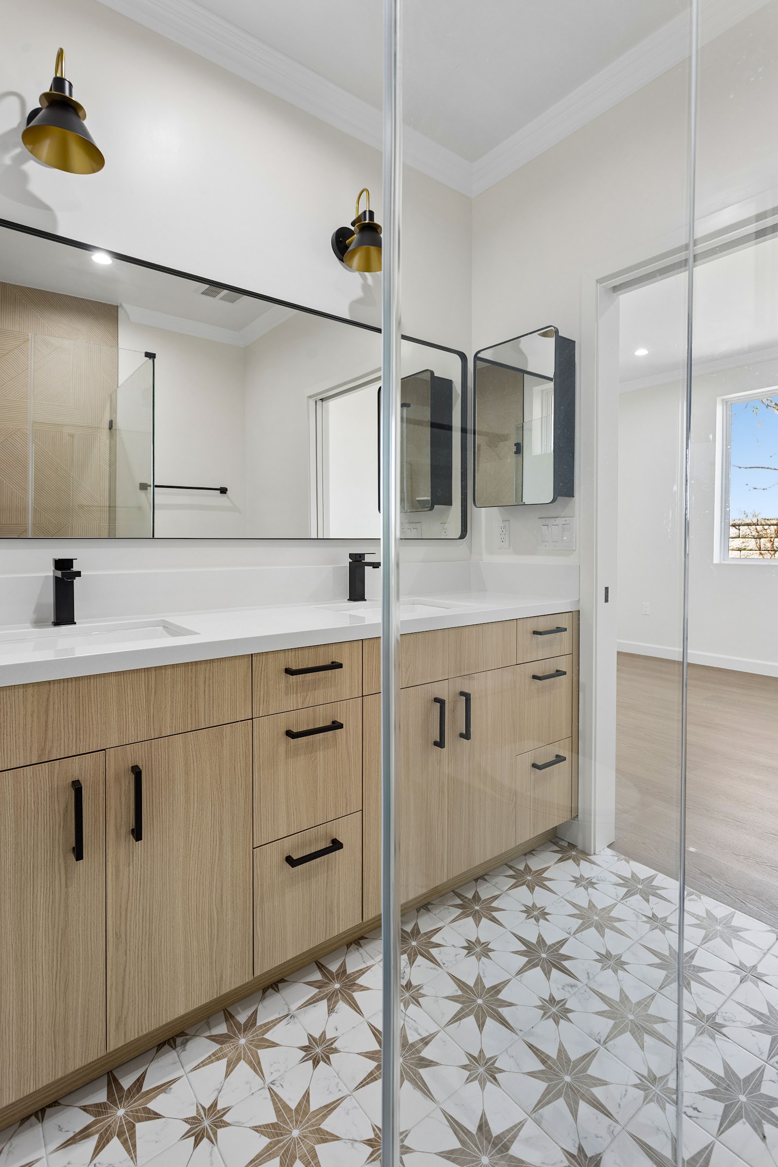 ADU bathroom with twin mirrors and a brass sconce above an oak vanity