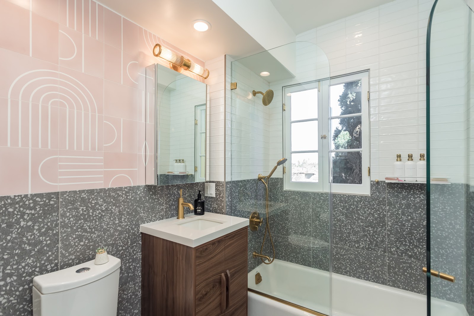 Bathroom remodel with grey terrazzo tile, blush patterned tile and brass fixtures