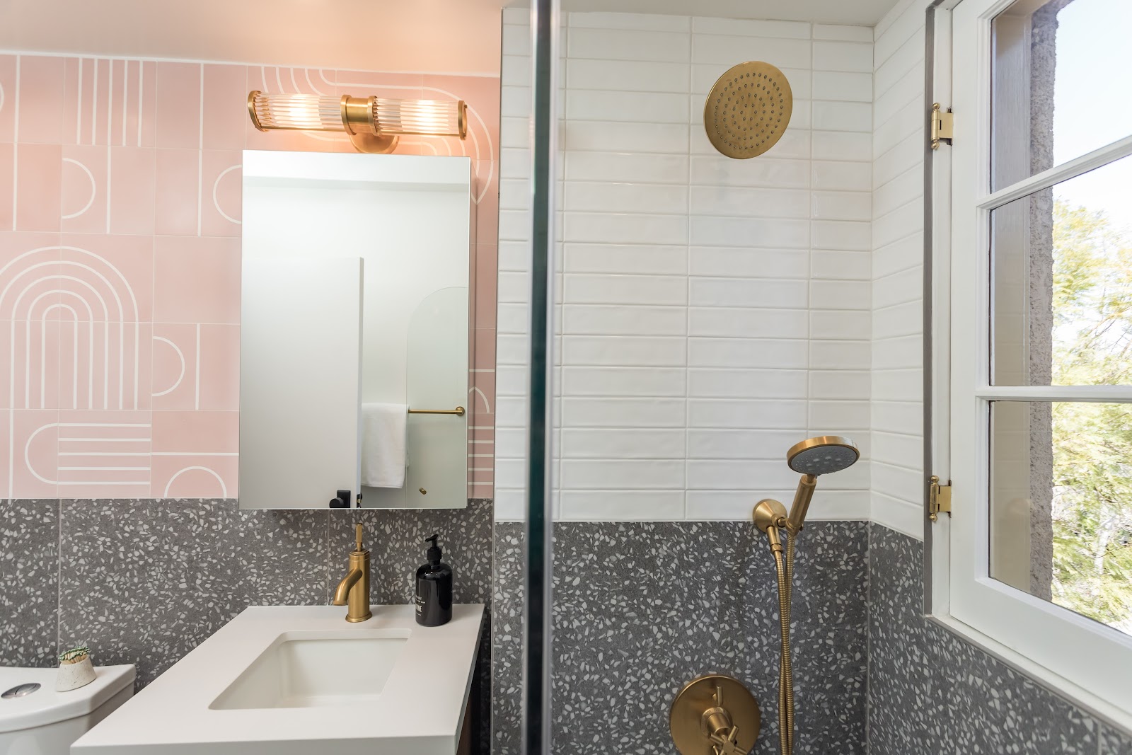 Bathroom vanity with a brass sconce, blush tile and terrazzo wainscot