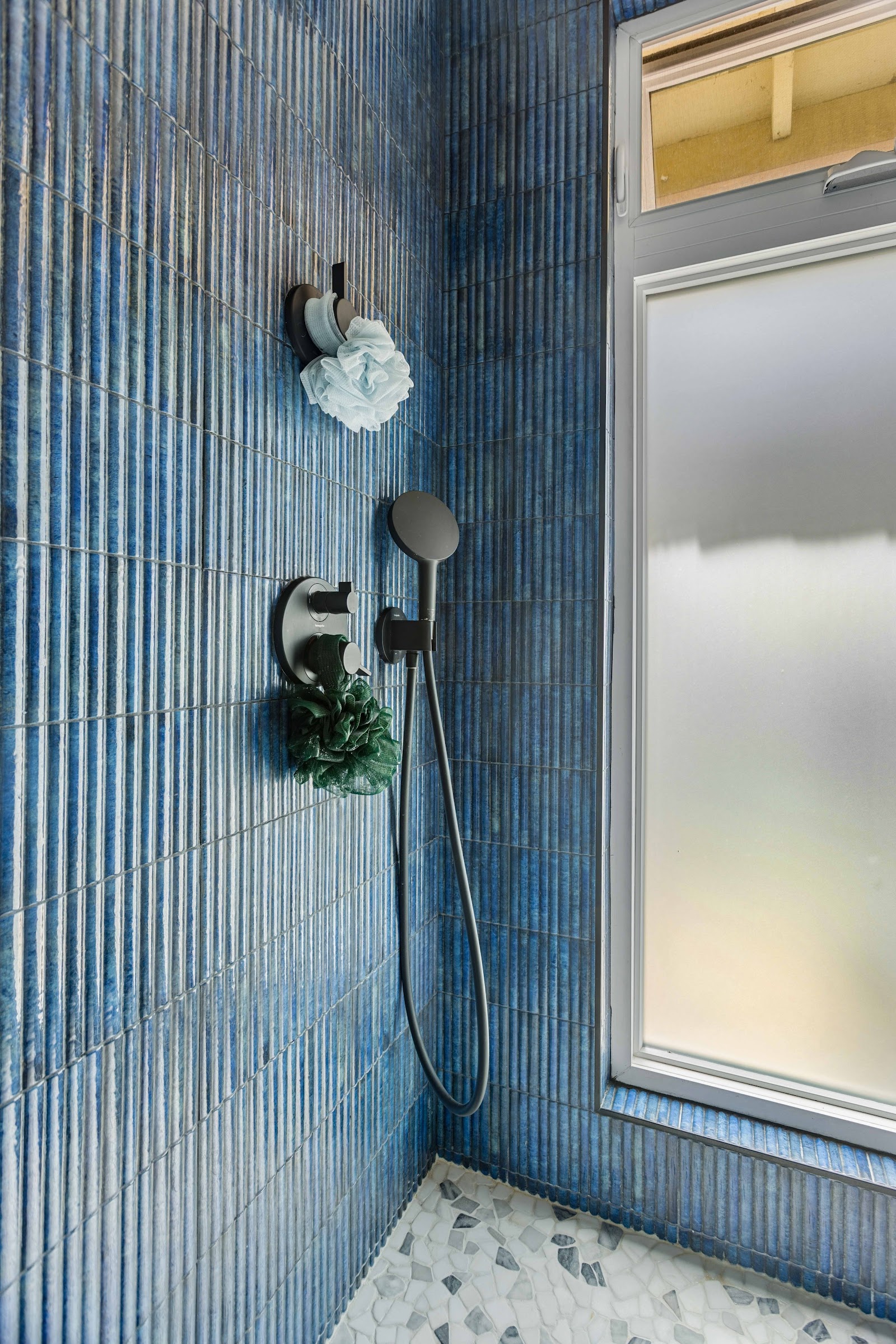 Blue fluted tile shower with matte black fixtures and a pebble floor