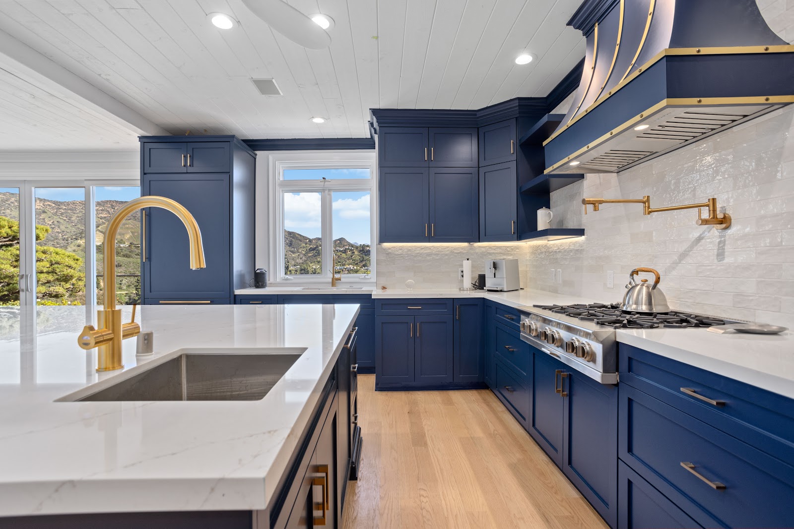 Brass gooseneck faucet on a waterfall island in a navy kitchen