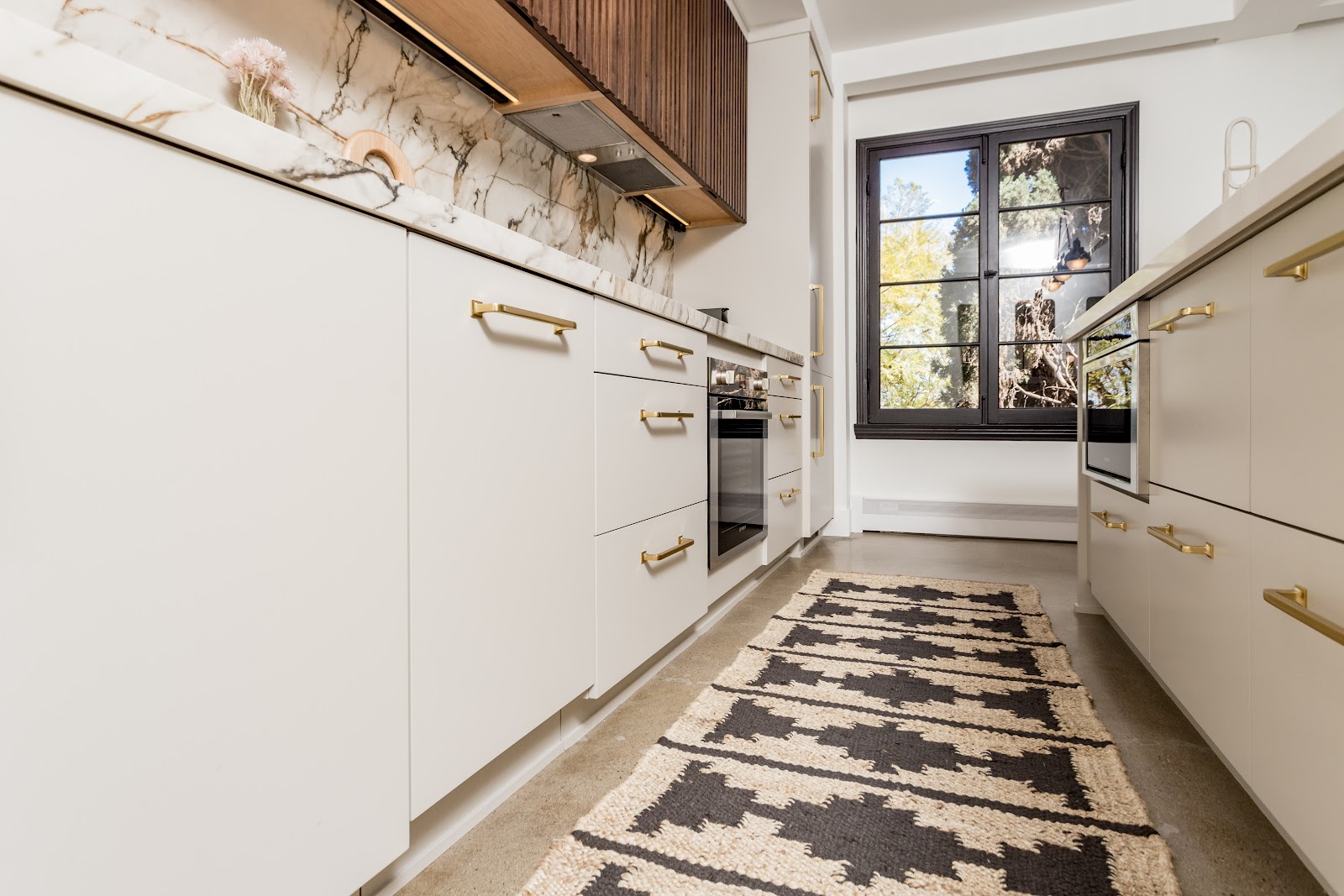 Butler pantry with brass bar pulls, marble counter and built-in ovens