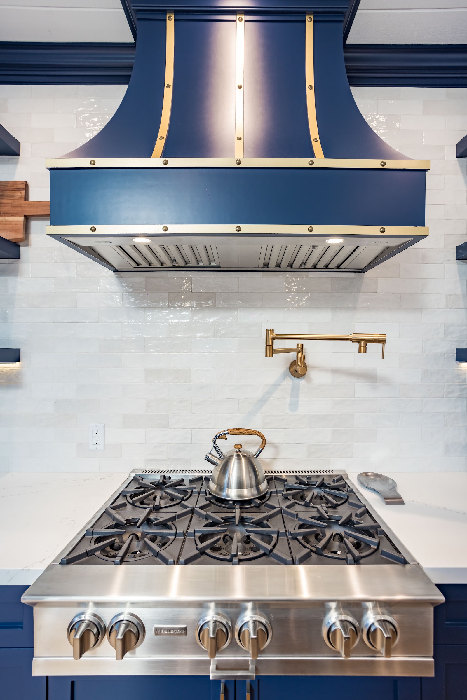 Range hood and pot filler against a pale stone backsplash