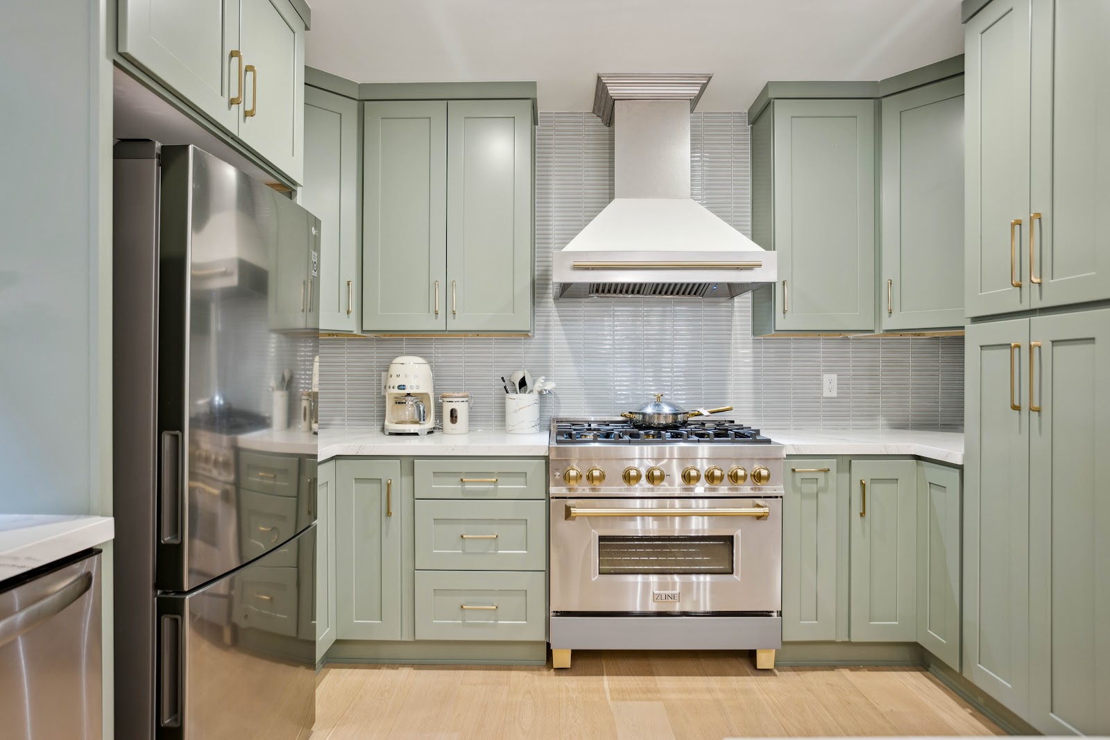 Sage shaker cabinets with a white plaster hood over a professional range