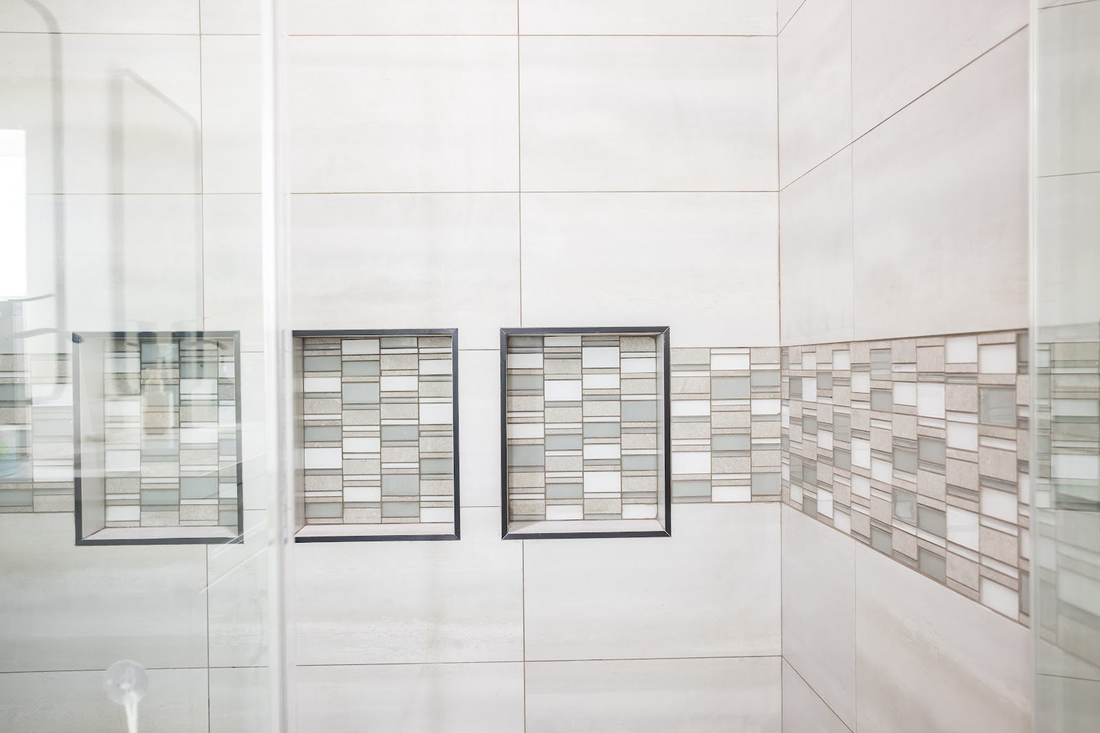 Large format shower tile with a glass mosaic band and recessed niches