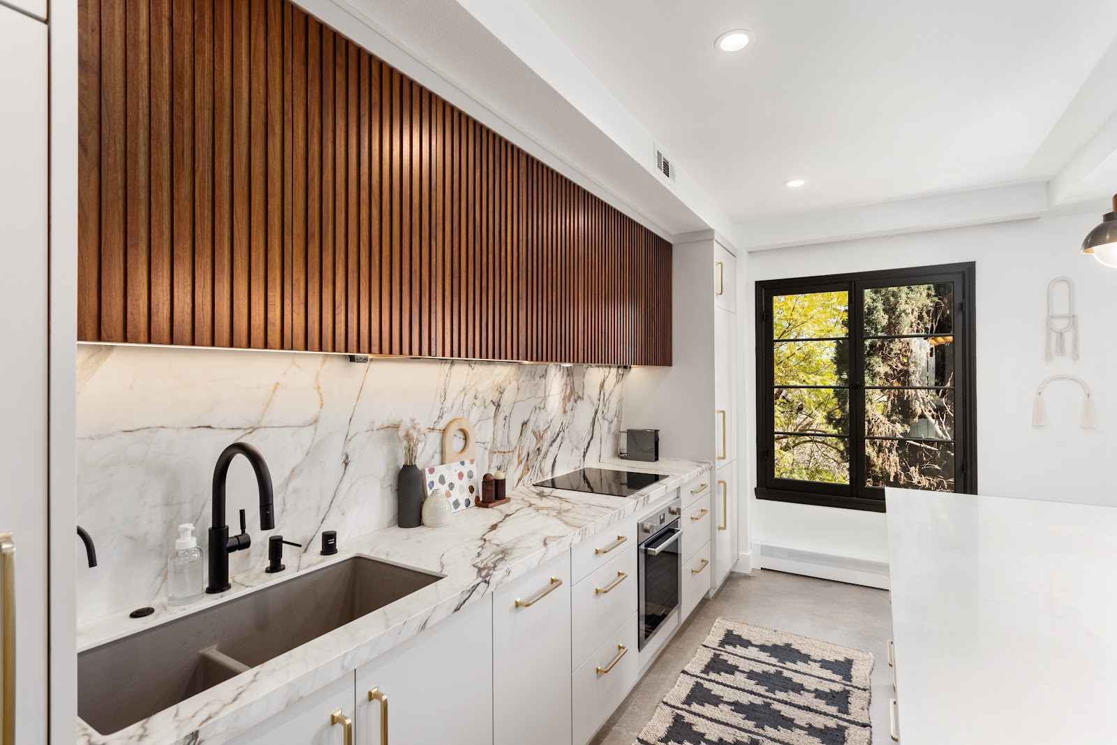 Walnut slat cabinets running to a black steel window in a remodeled kitchen