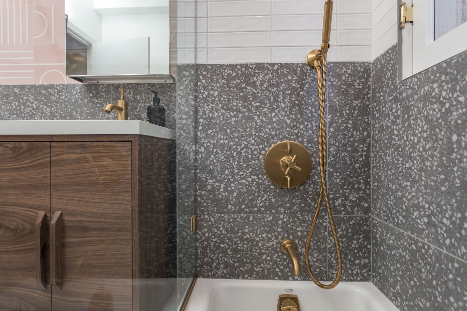 Walnut floating vanity beside a grey terrazzo shower with brass fittings